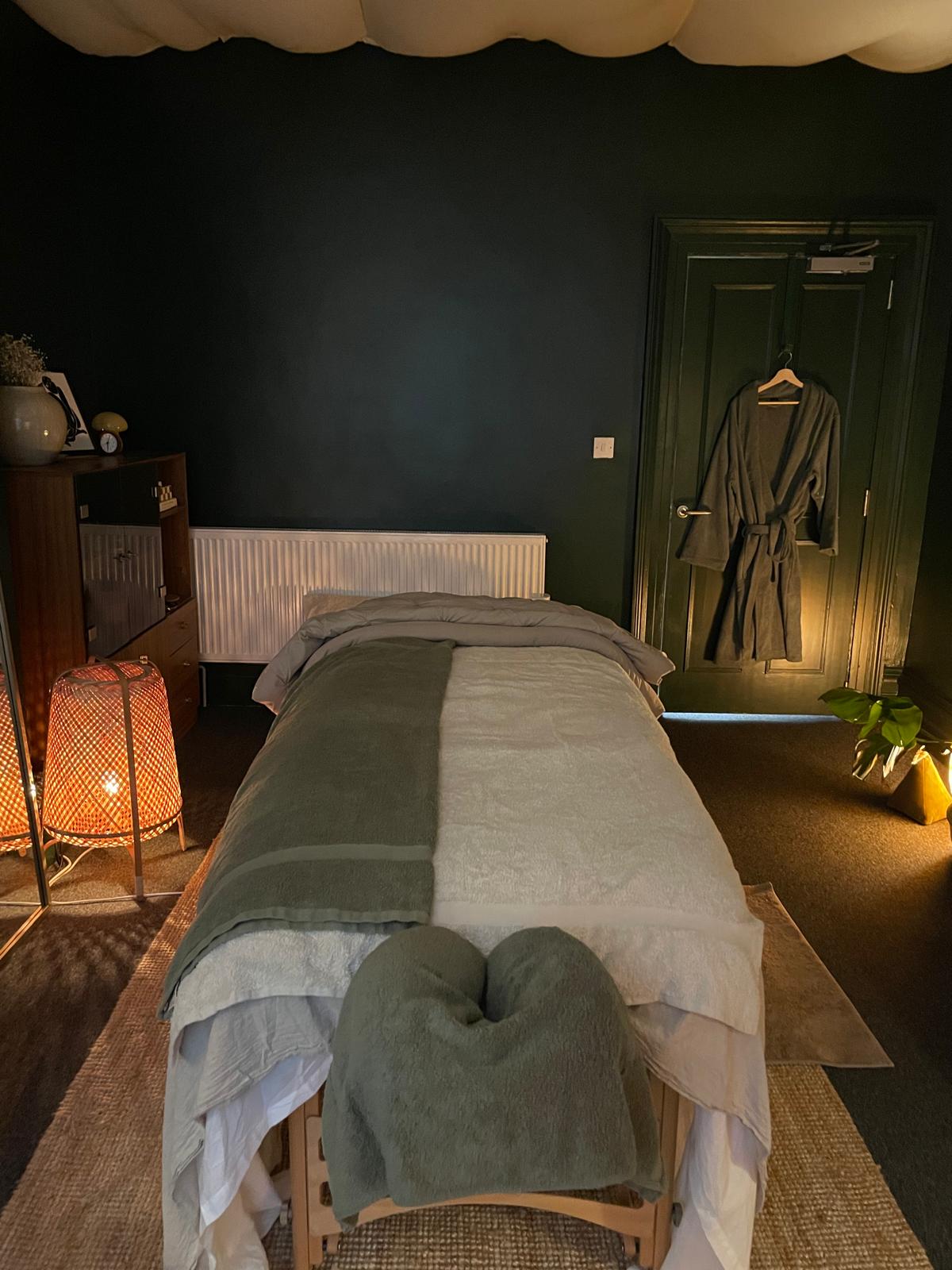 Massage table with sage bedding, robe hanging by the door.